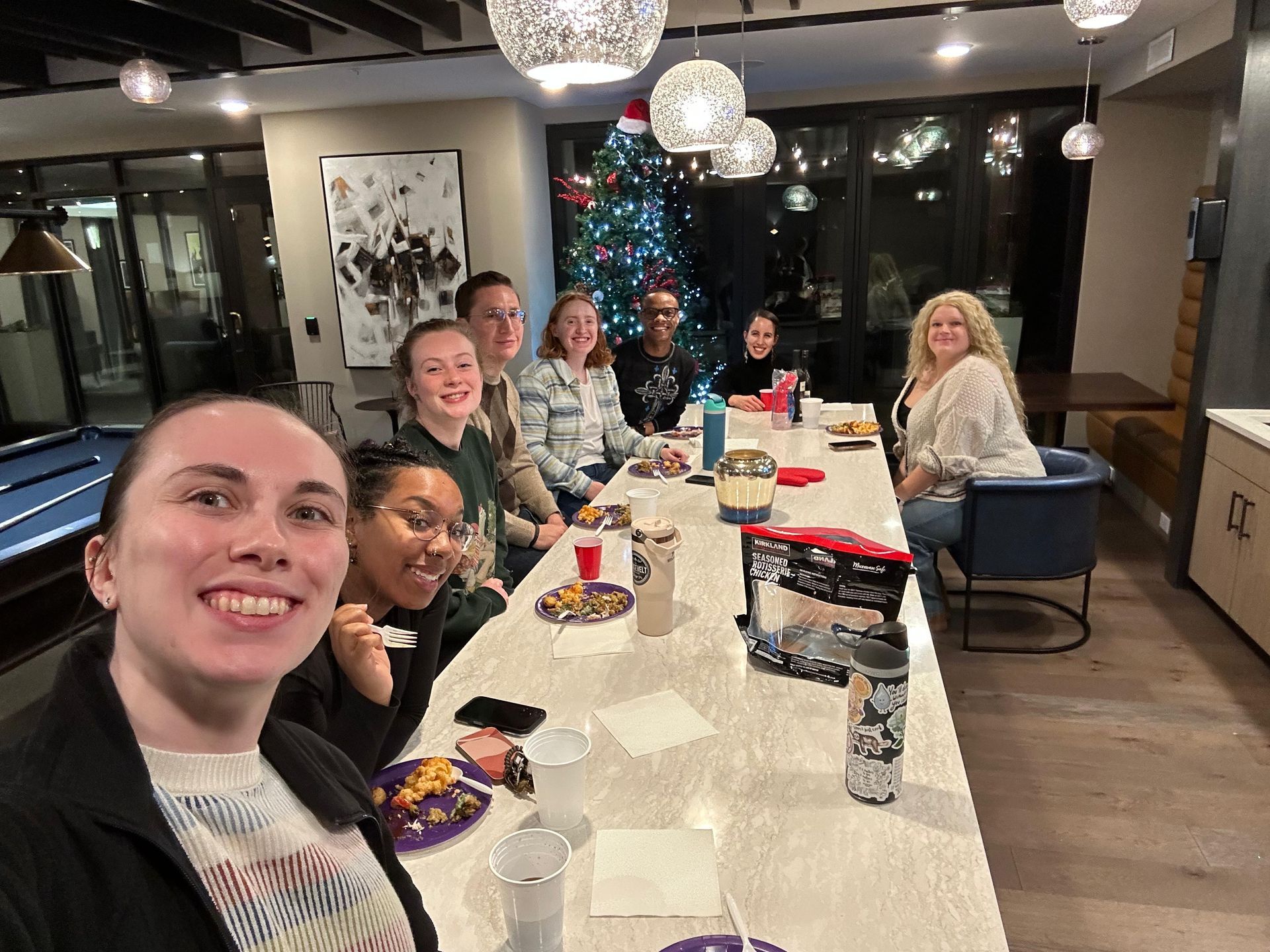 Short North Church. People gathered around a long table in a bright room, smiling for a group selfie beside a decorated tree.