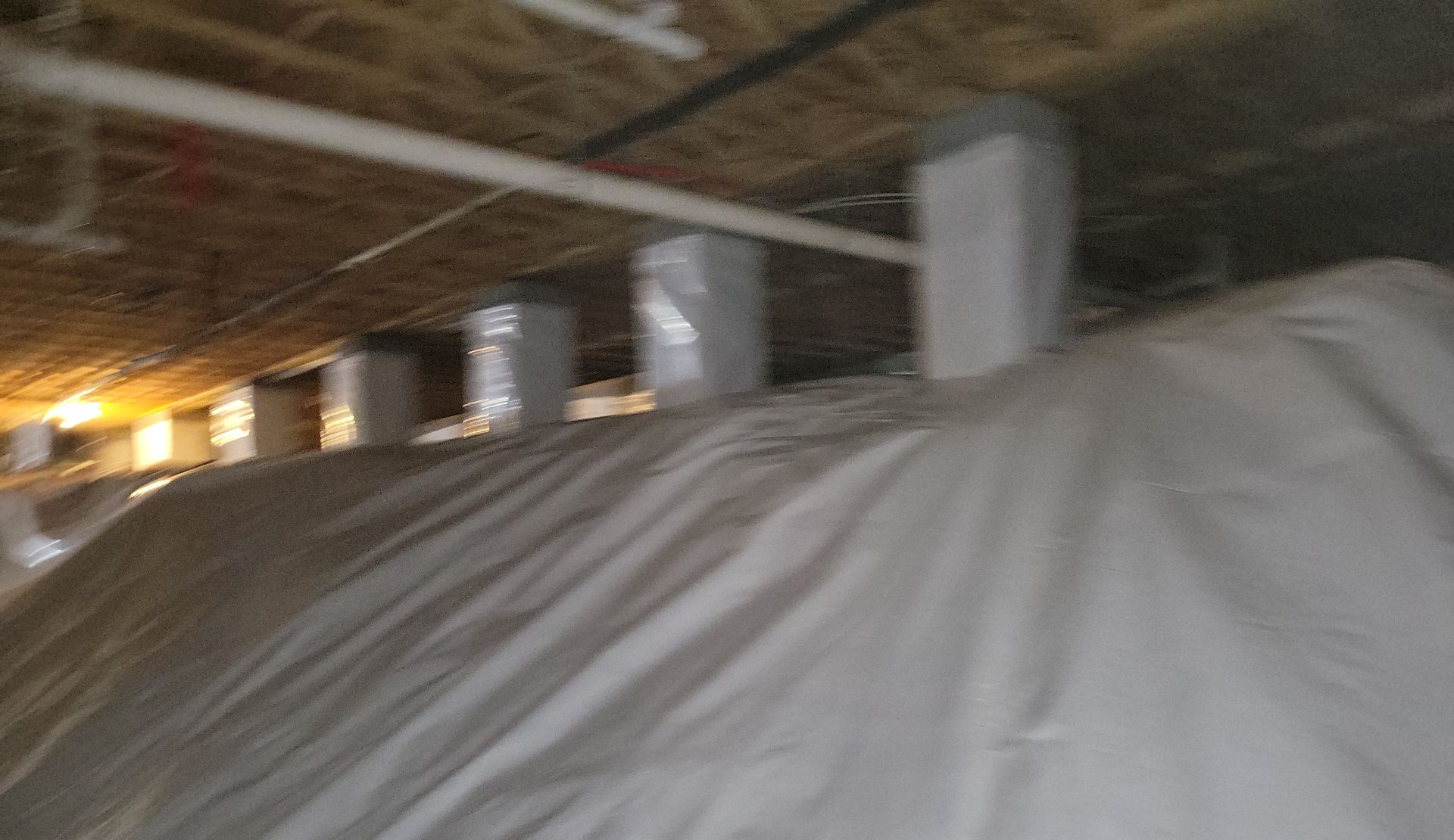 Interior view of a crawl space with white insulation and ductwork visible, some wrapped.
