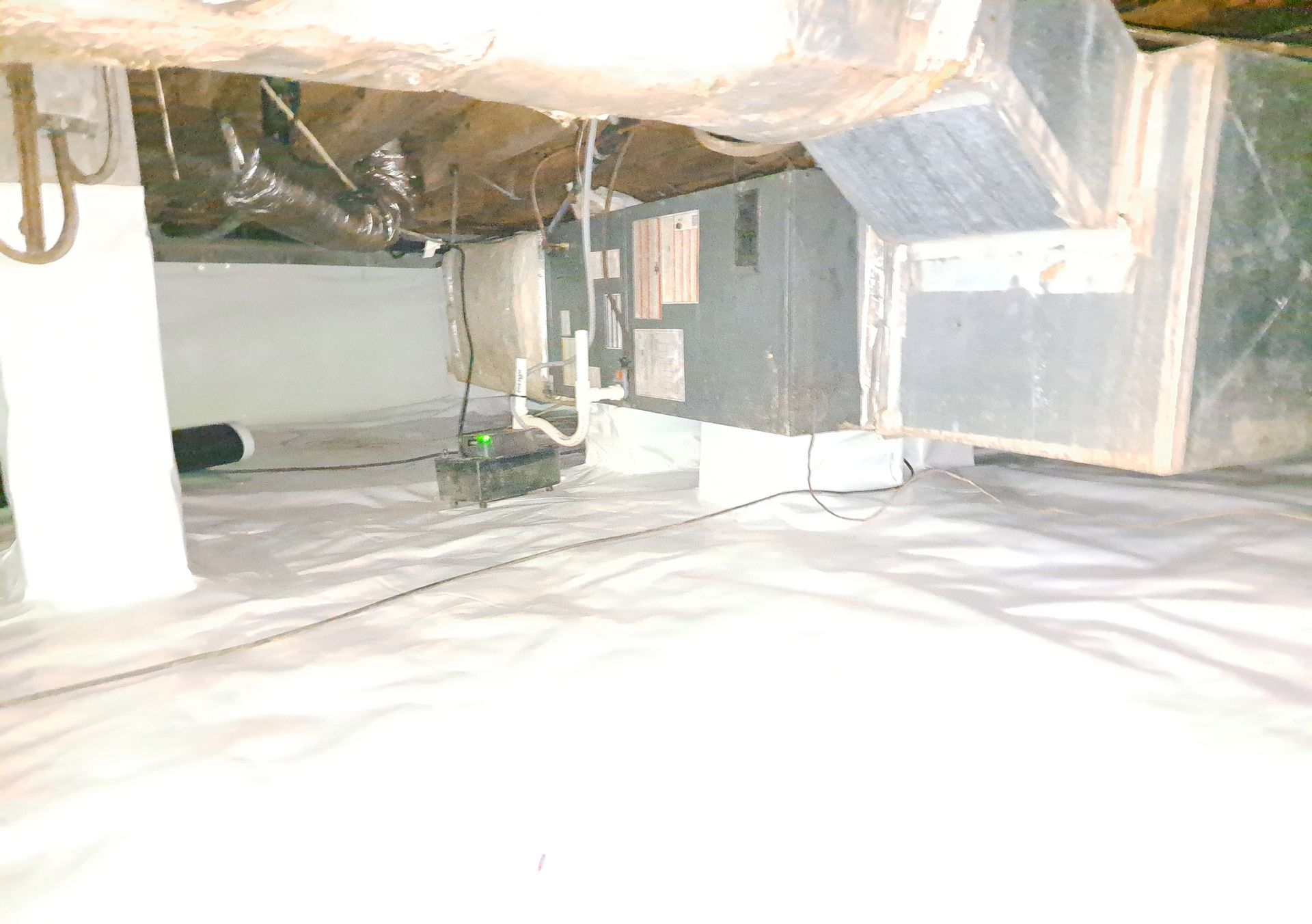 Crawl space with white vapor barrier. HVAC system, ductwork, and support beams visible.