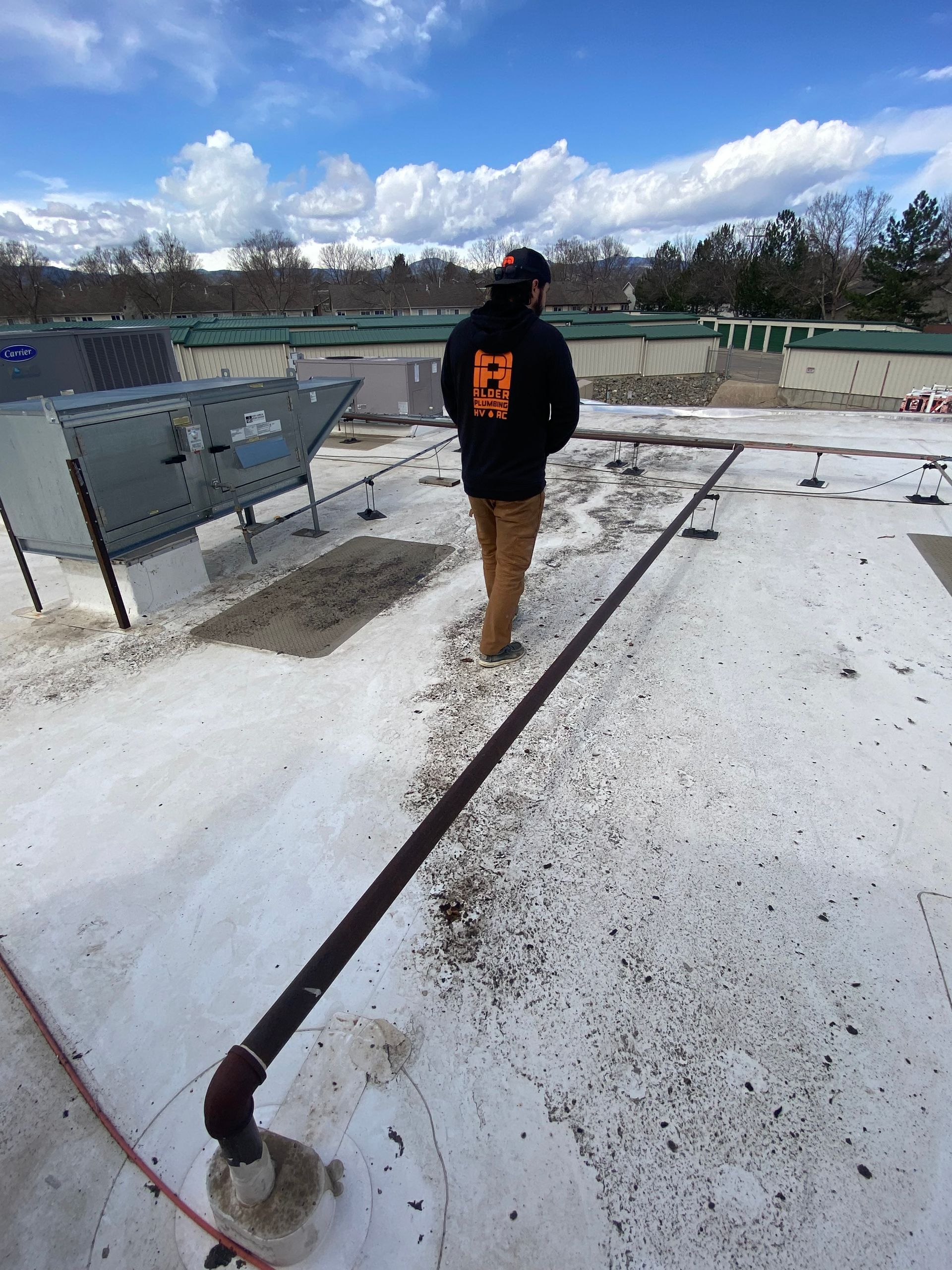 Person on a rooftop, wearing a dark jacket, brown pants.  A line of debris runs across the white roof.