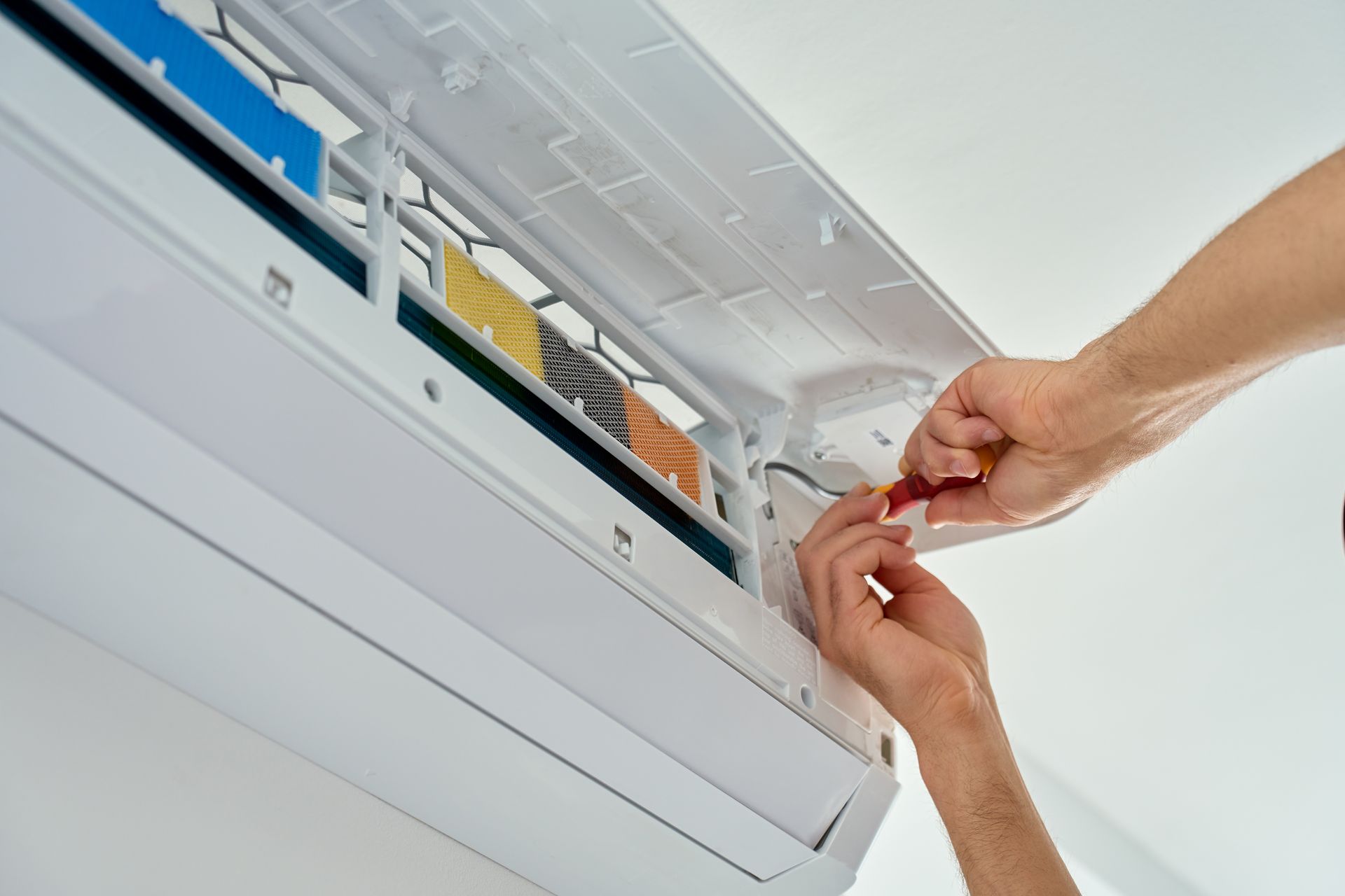 Hand repairs an open wall air conditioner with a screwdriver.
