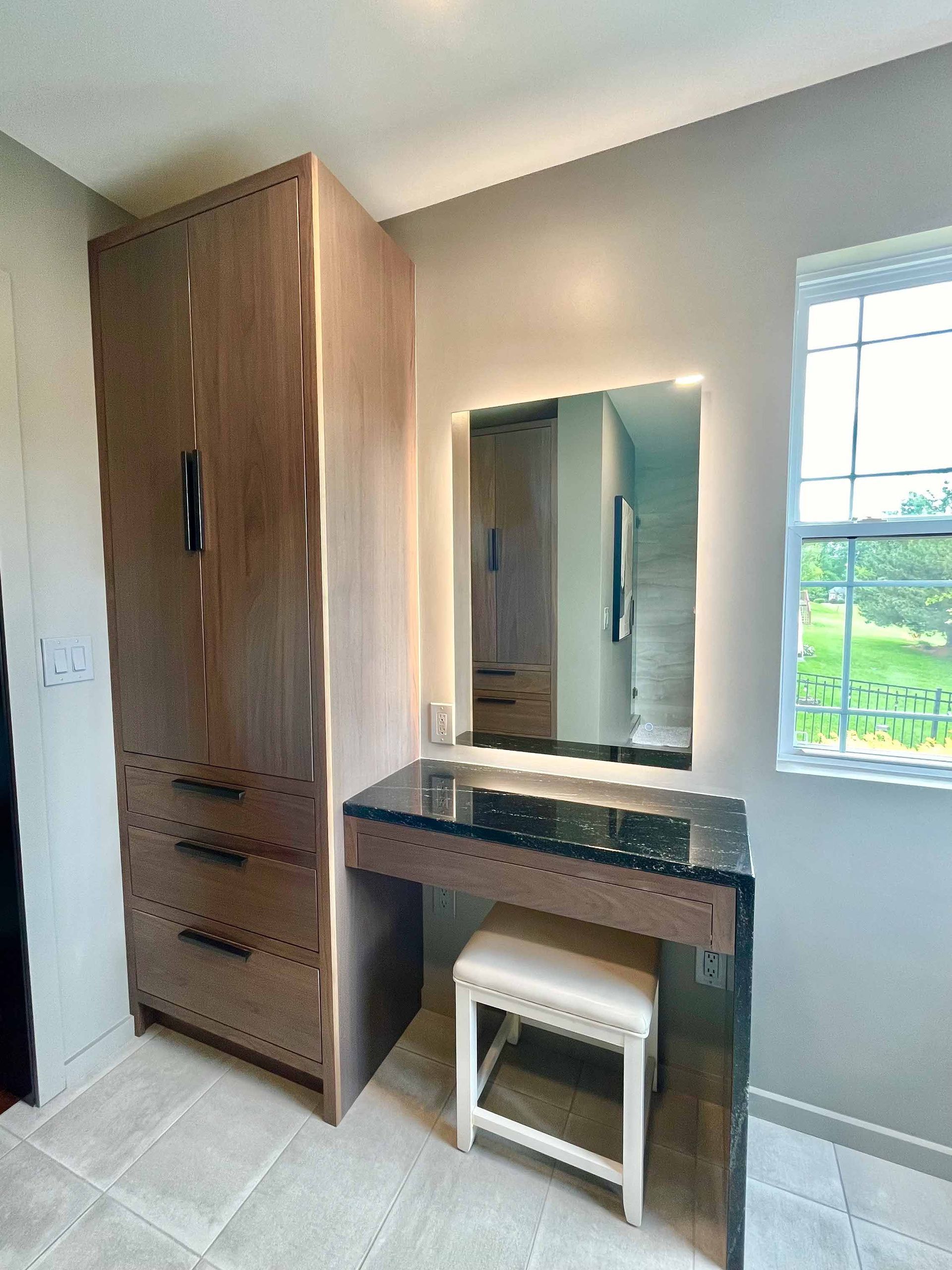 A bedroom with a vanity , mirror , stool and wardrobe.
