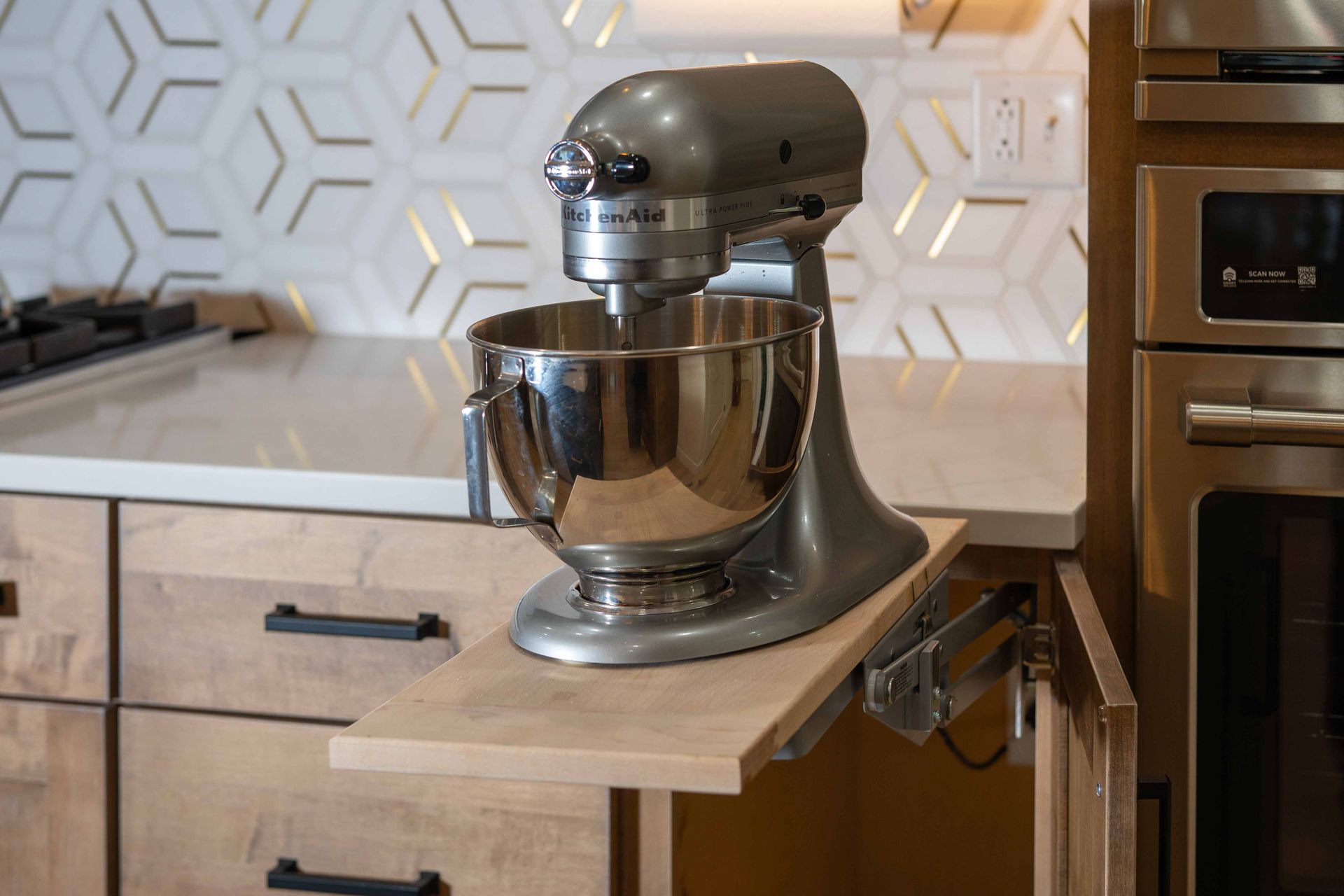 A kitchenaid mixer is sitting on a wooden shelf in a kitchen.