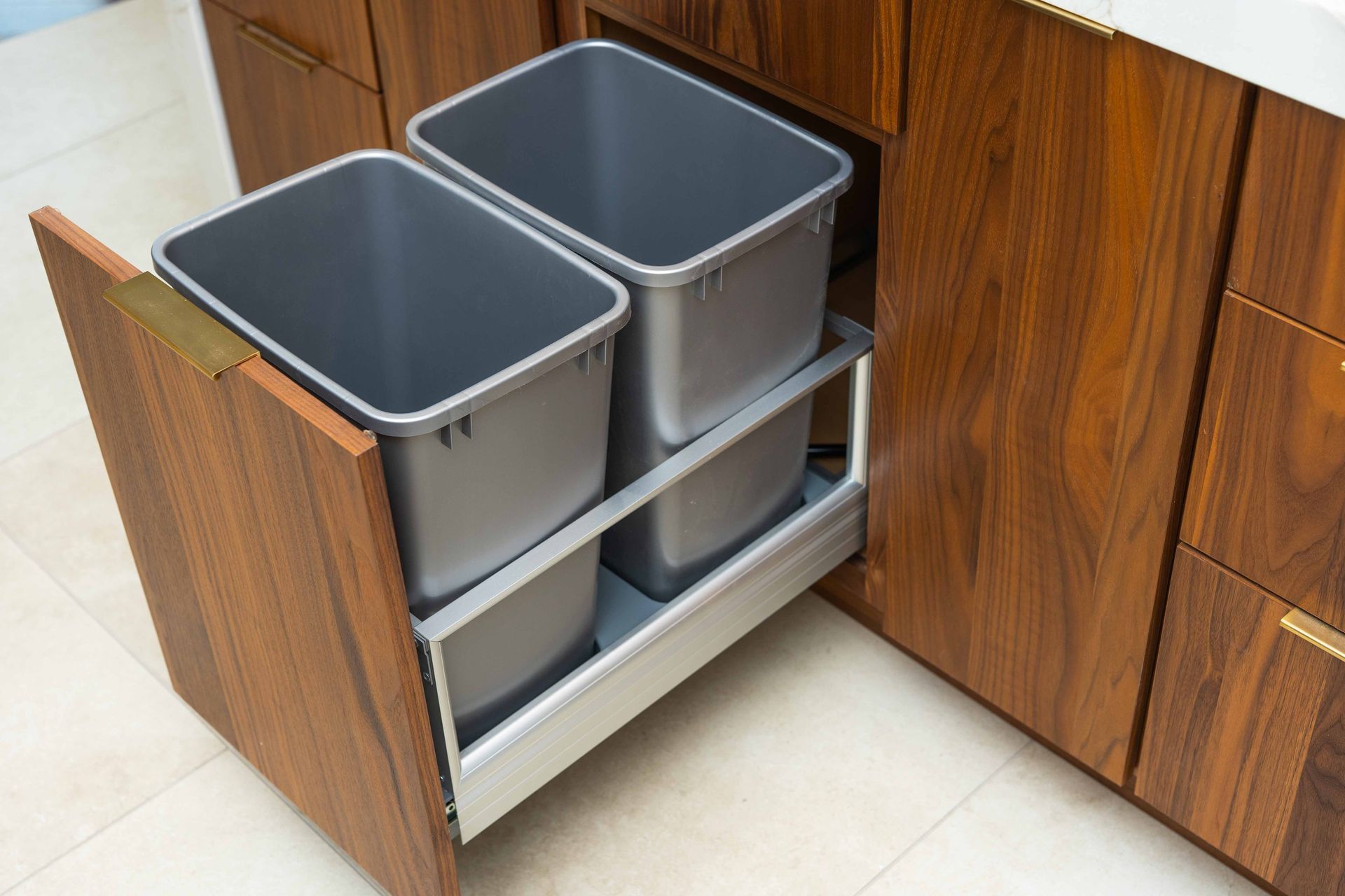 Two trash cans are pulled out of a drawer in a kitchen.