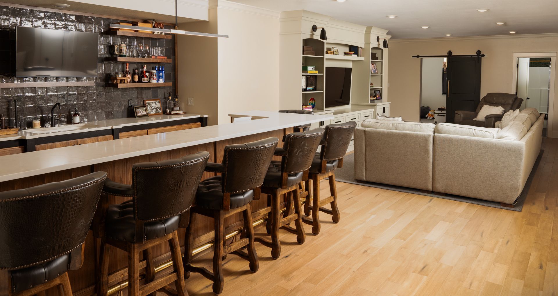 A living room with a bar and stools and a couch.