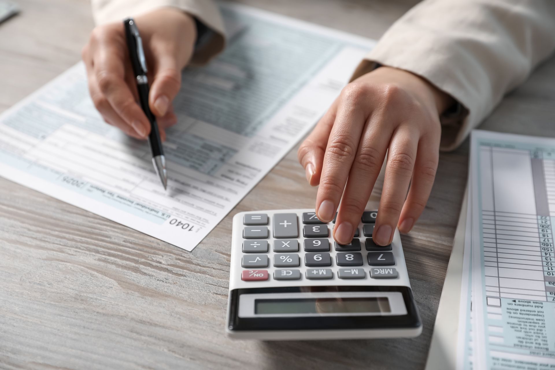 Hands using a calculator and pen on financial documents on a desk