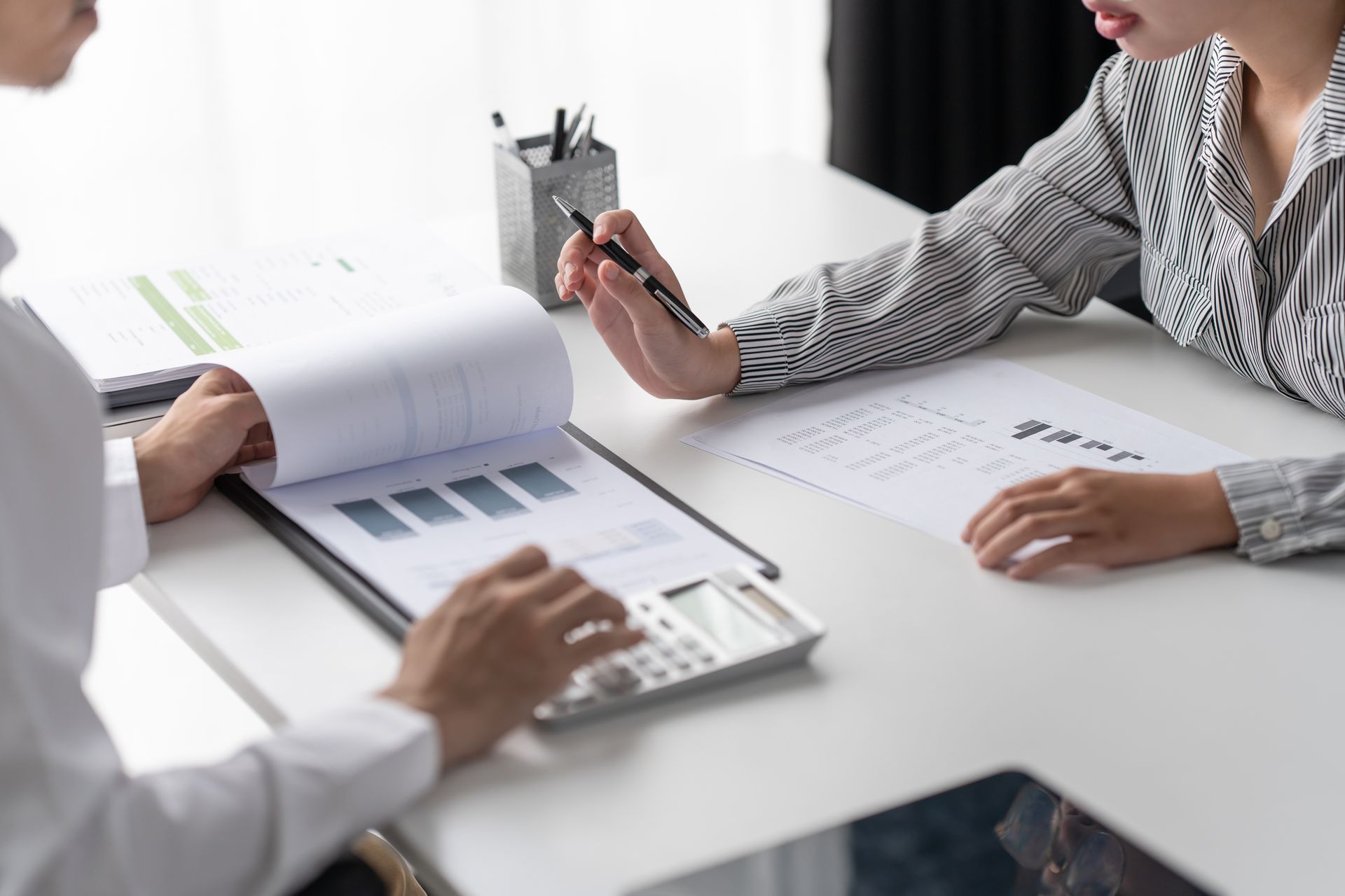 People reviewing documents at a desk, with one pointing at a chart on a clipboard.