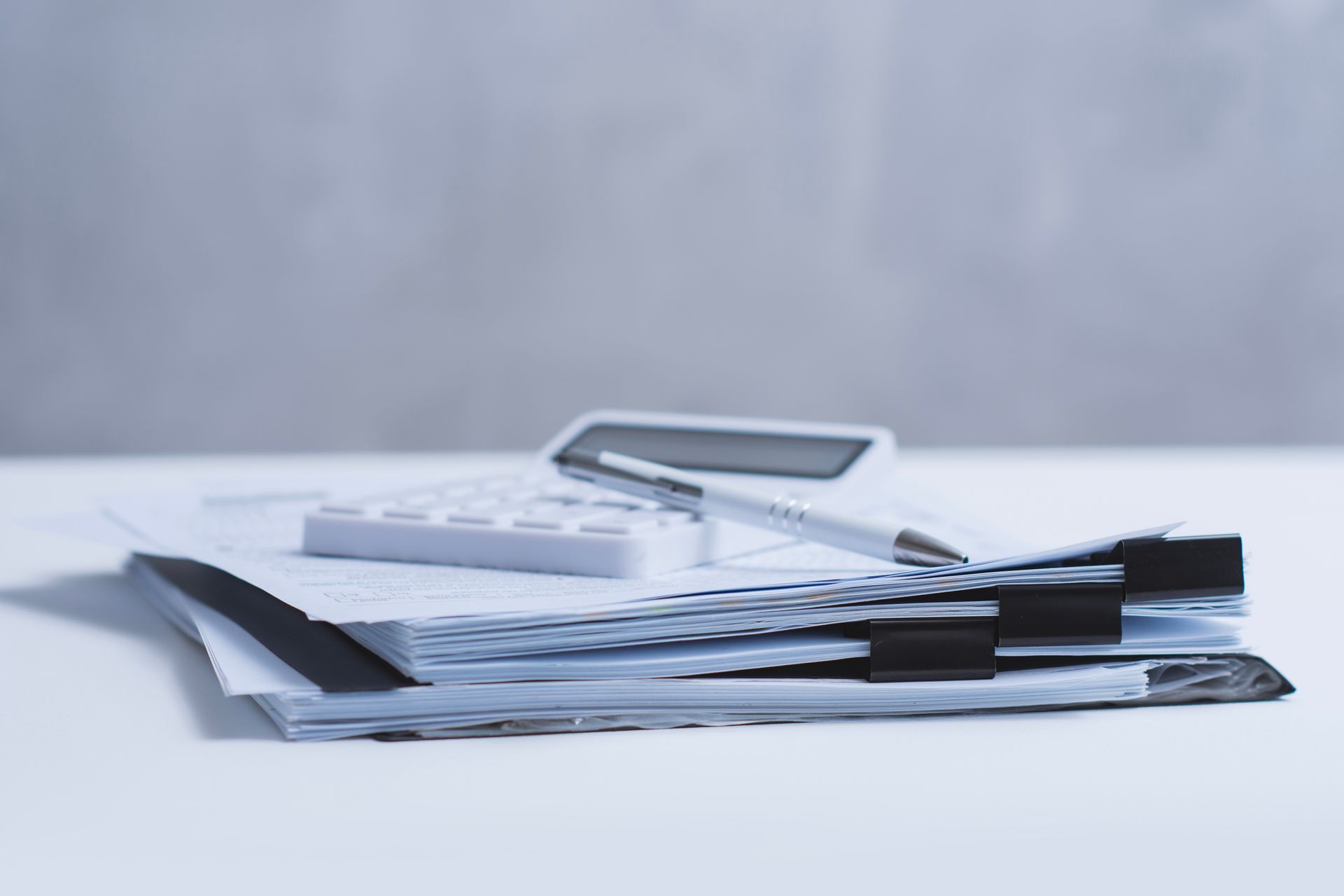 Calculator resting on a stack of paperwork and folders on a white desk