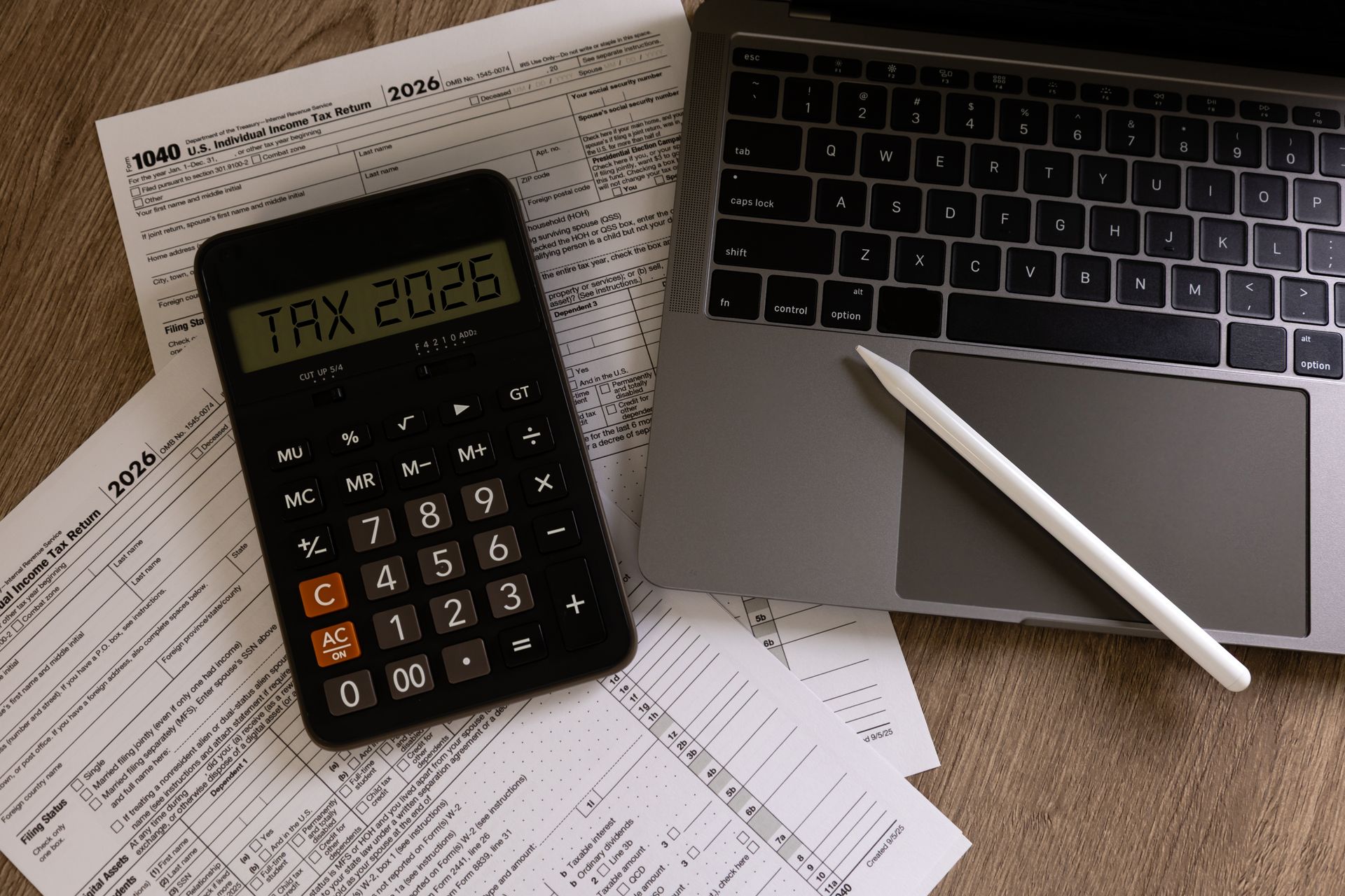 Calculator, laptop, stylus, and paperwork on a desk with printed documents scattered around.