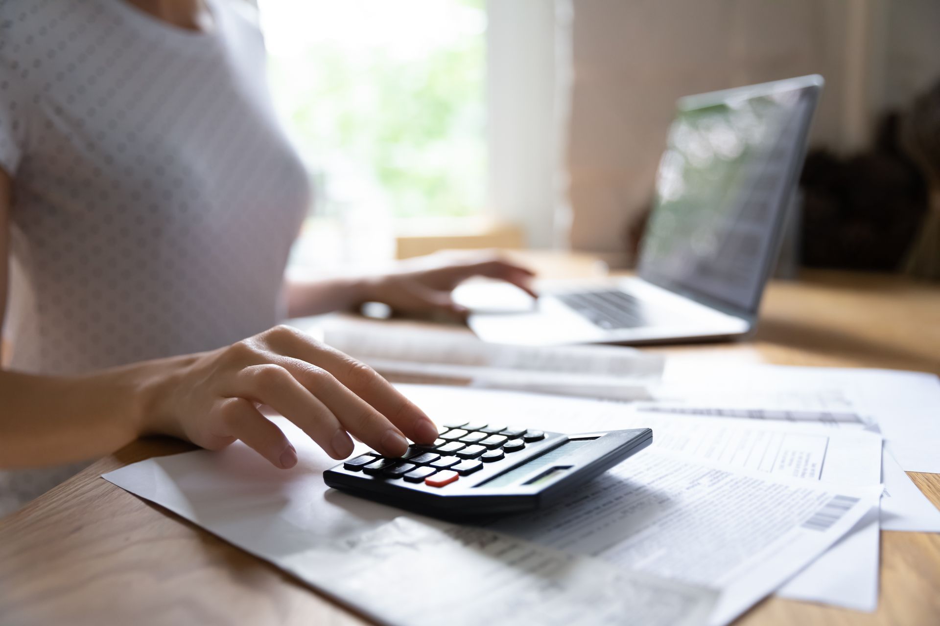 Person using a calculator at a desk with papers and a laptop nearby