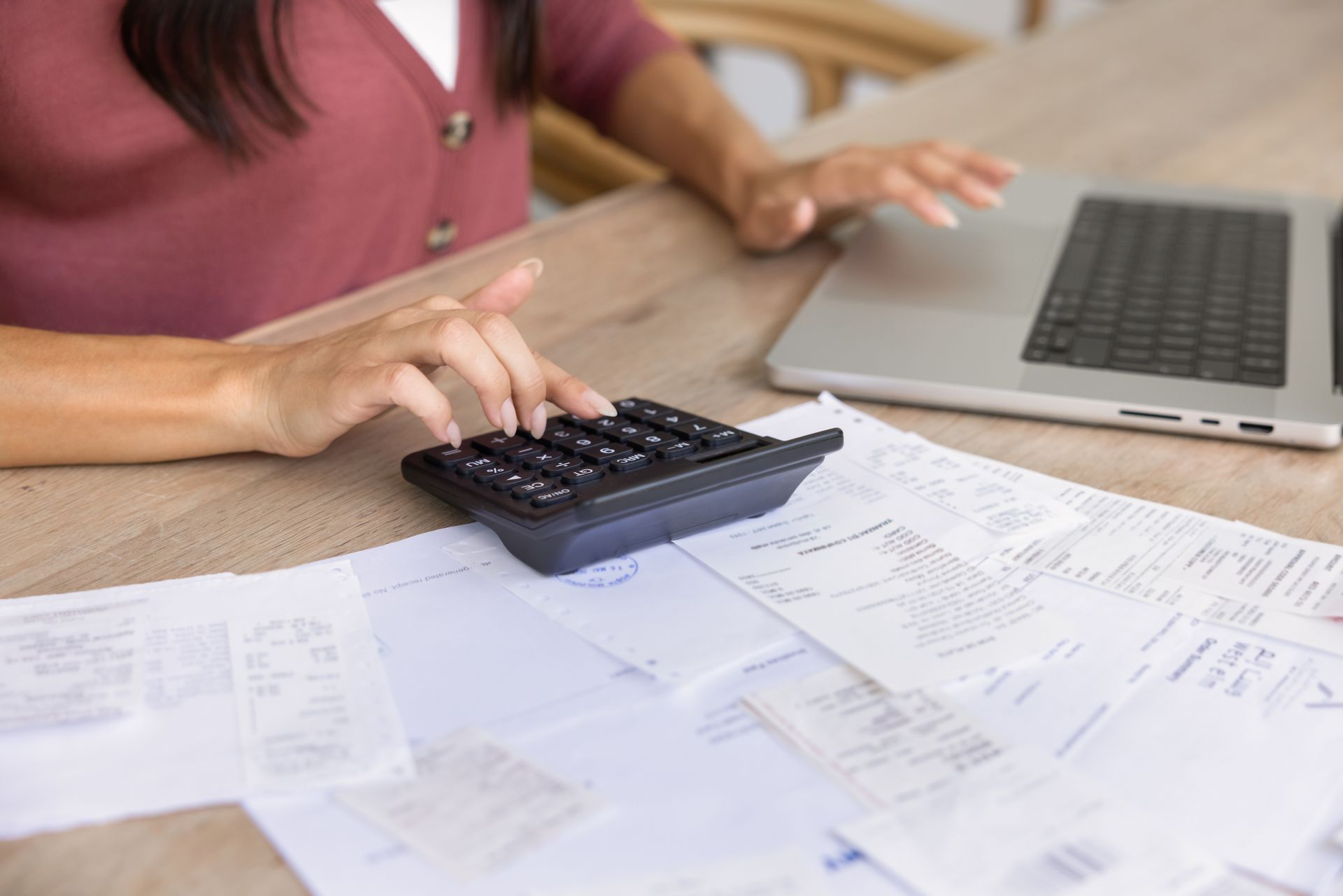 Hands using a calculator on papers beside a laptop at a desk