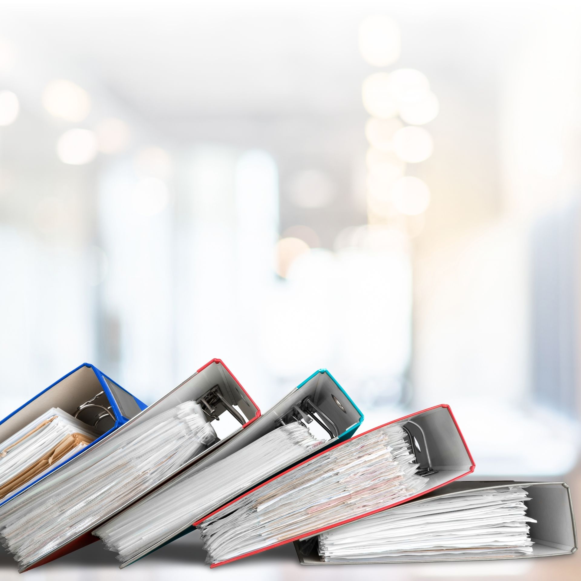 Stack of open binders with papers on a desk against a bright blurred office background