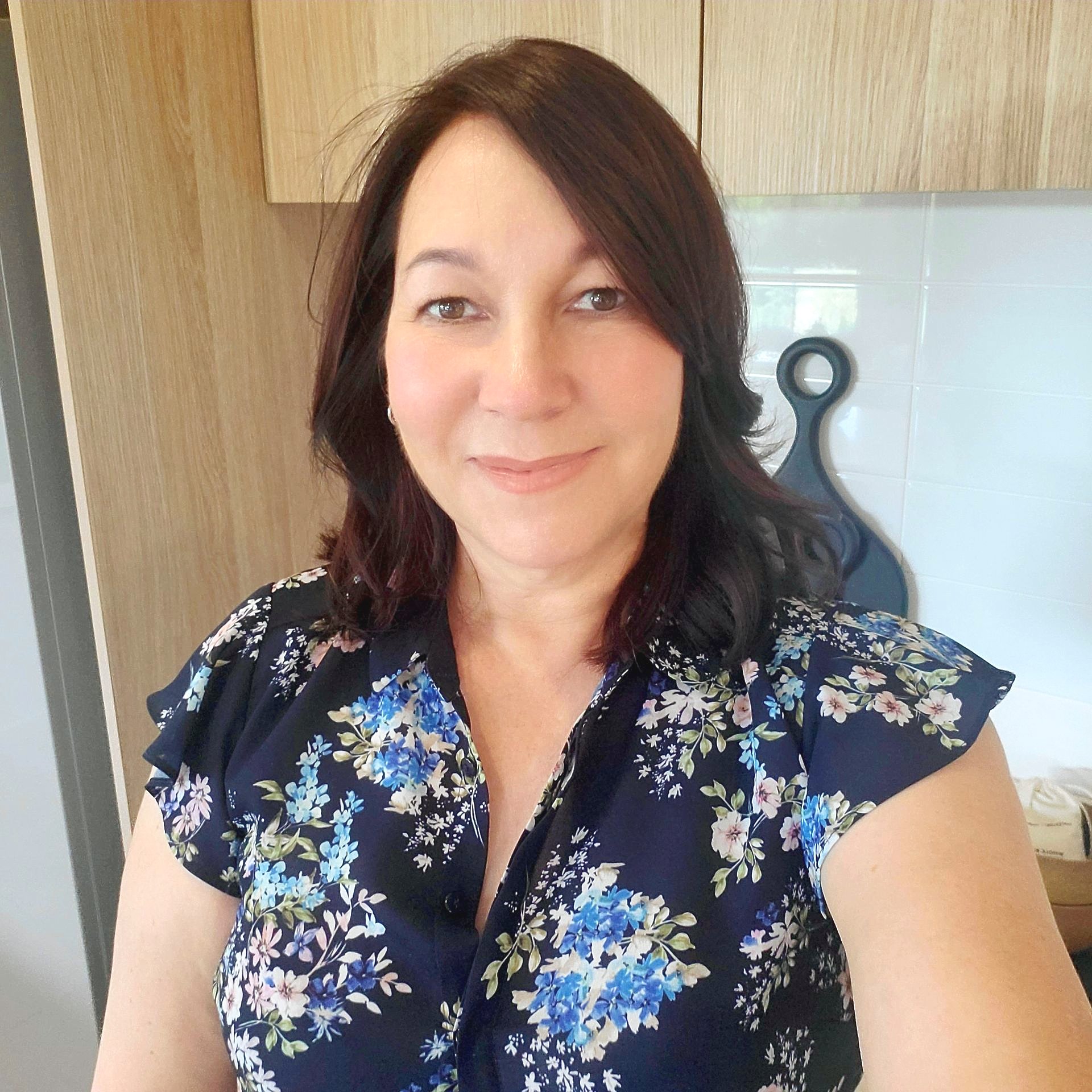 Woman in floral top smiles indoors, near wooden cabinets — Jodi Maree Interiors in Dubbo, NSW