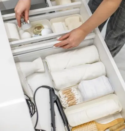 Person Organizing a White Bathroom Drawer With Towels, Toiletries, and Hair Styling Tools — Jodi Maree Interiors in Dubbo, NSW