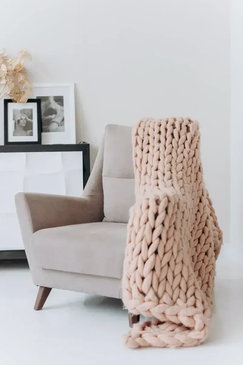 Beige Knitted Blanket Draped Over a Beige Armchair in a Light-filled Room — Jodi Maree Interiors in Dubbo, NSW