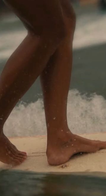 Two bare feet on a surfboard with waves breaking in the background — Holiday Sun Swimwear on the Gold Coast, QLD