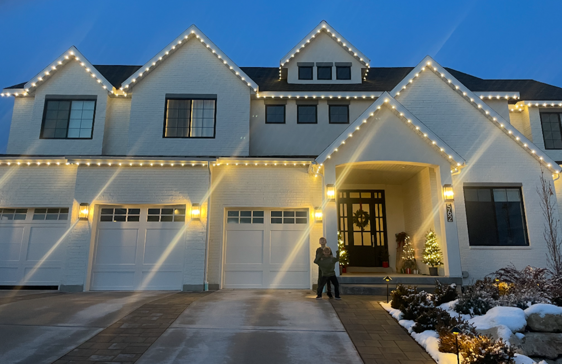White house with Christmas lights. Night. Person standing in the driveway.