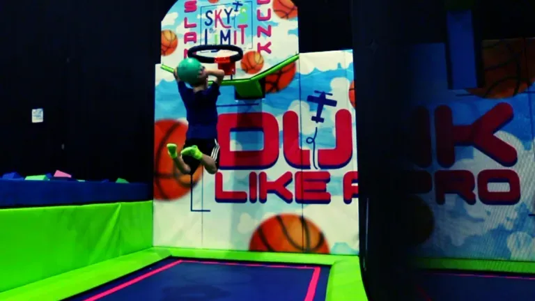Boy jumping on a trampoline, attempting to dunk a ball. Basketball hoop and