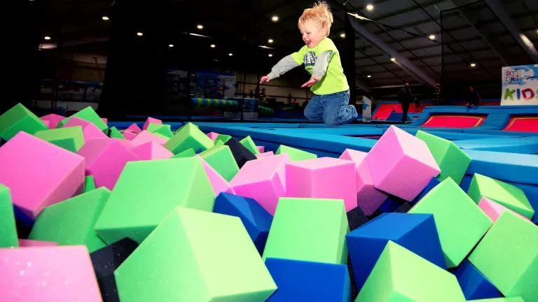 Child jumping into a foam pit at an indoor trampoline park; colorful cubes and trampolines.