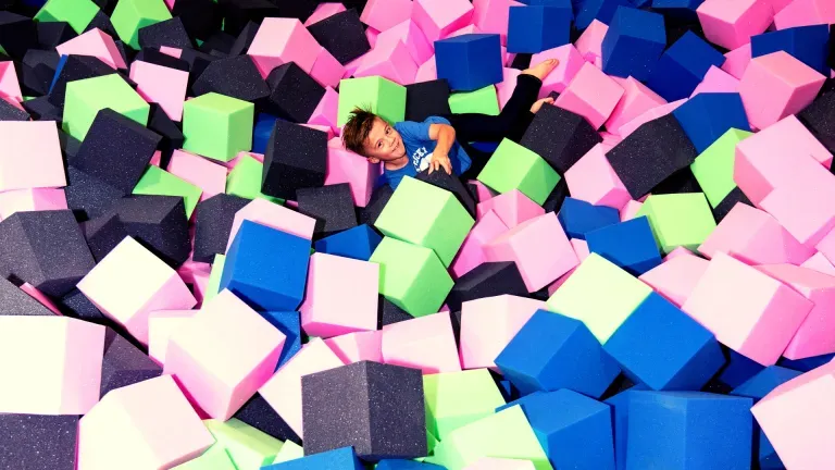 Boy in a foam pit, surrounded by blue, pink, green, and black foam cubes.