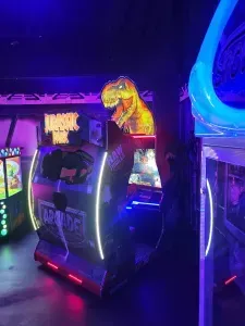Dinosaur-themed arcade game with neon lights in a dimly lit arcade. A T-Rex head is on top.