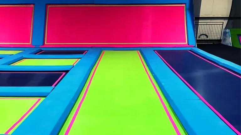 Indoor trampoline park with neon green, blue, and pink trampolines and wall padding.
