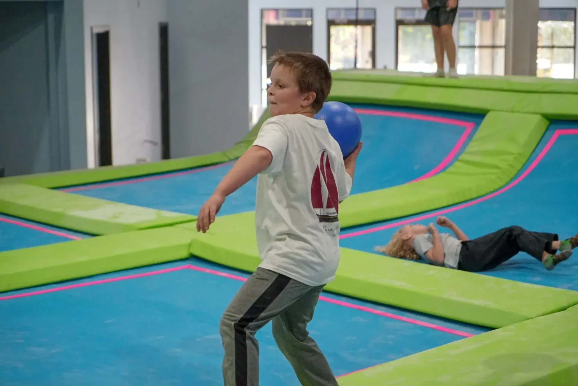 Boy throws blue ball on trampoline with other people.