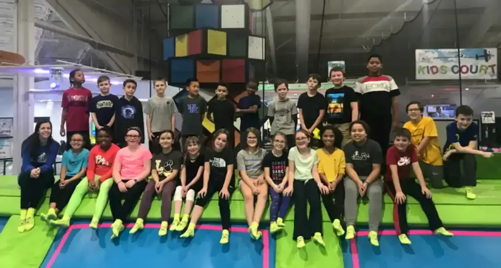 Group of people posing on a trampoline with colorful blocks in the background. Many wearing neon socks.