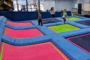 Children jumping on colorful trampolines in an indoor recreation area.