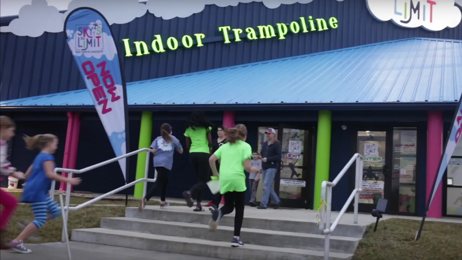 Children running into a trampoline park with green and blue facade. 