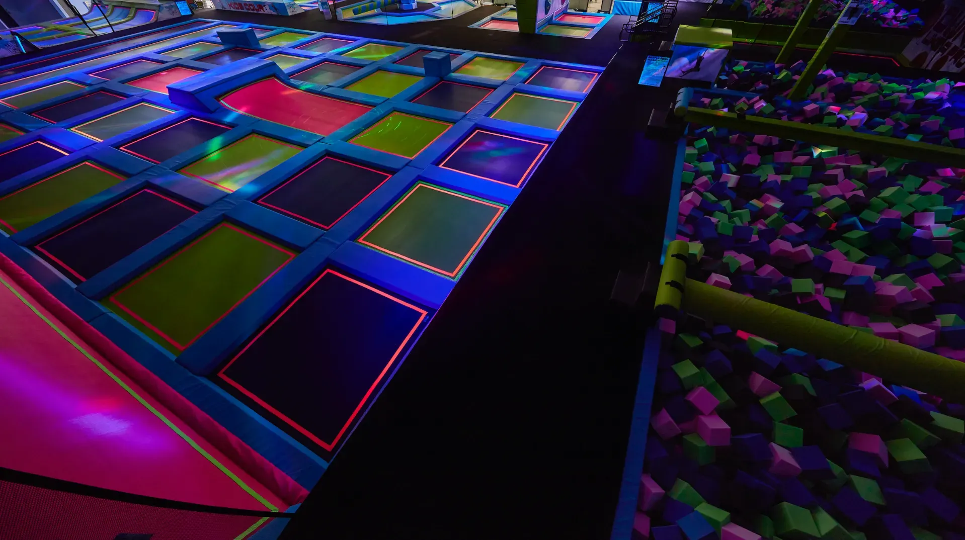 Indoor trampoline park with colorful illuminated trampolines and foam pit.