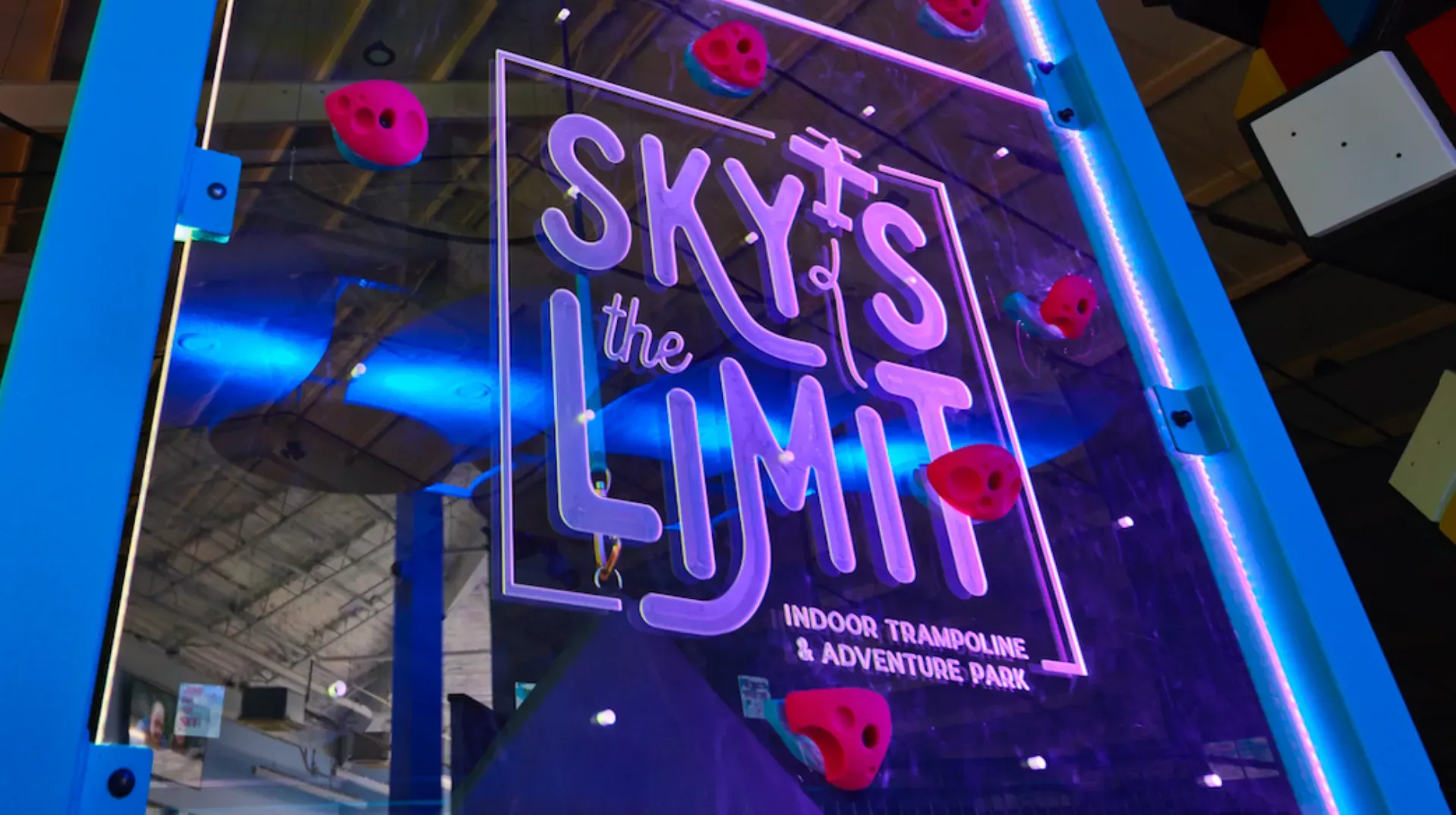 Sign for Sky's the Limit Adventure Park. Blue and white sign, with red climbing holds.