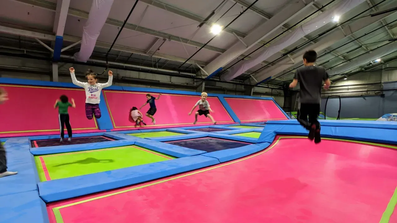 People jumping on trampolines in an indoor trampoline park; pink, blue, green mats.