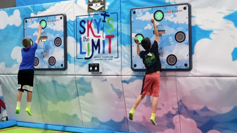 Two boys jumping and reaching for targets on a climbing wall at Sky's the Limit, an indoor trampoline park.