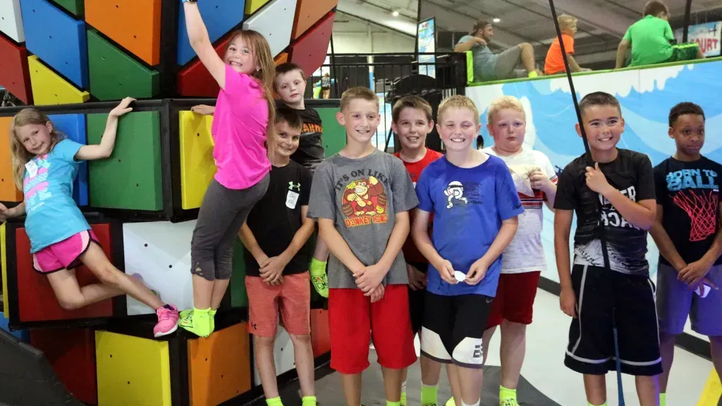 Group of children posing at an indoor playground with colorful climbing walls.