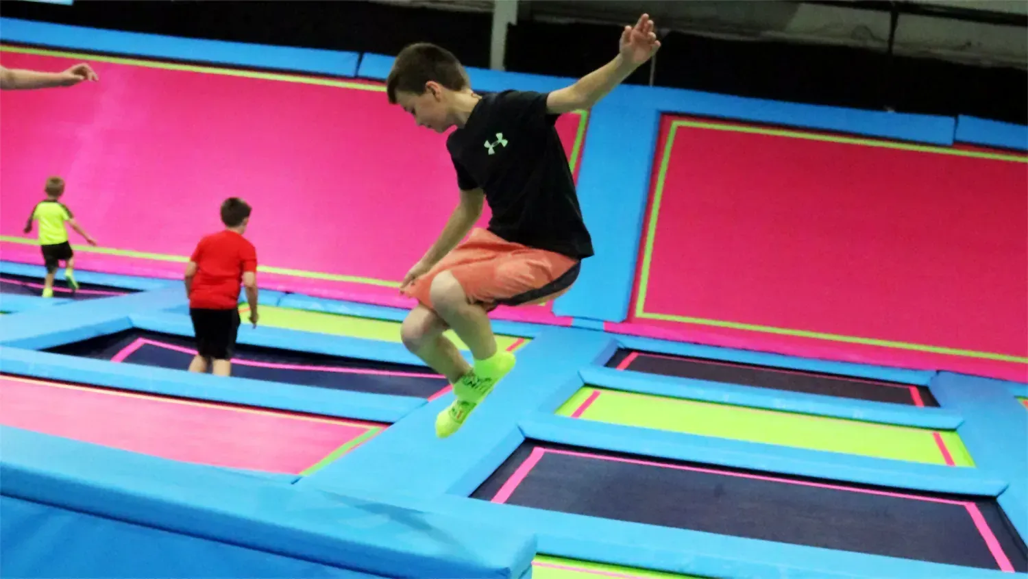 Boy jumping on a trampoline, with other people in the background, in an indoor trampoline park.