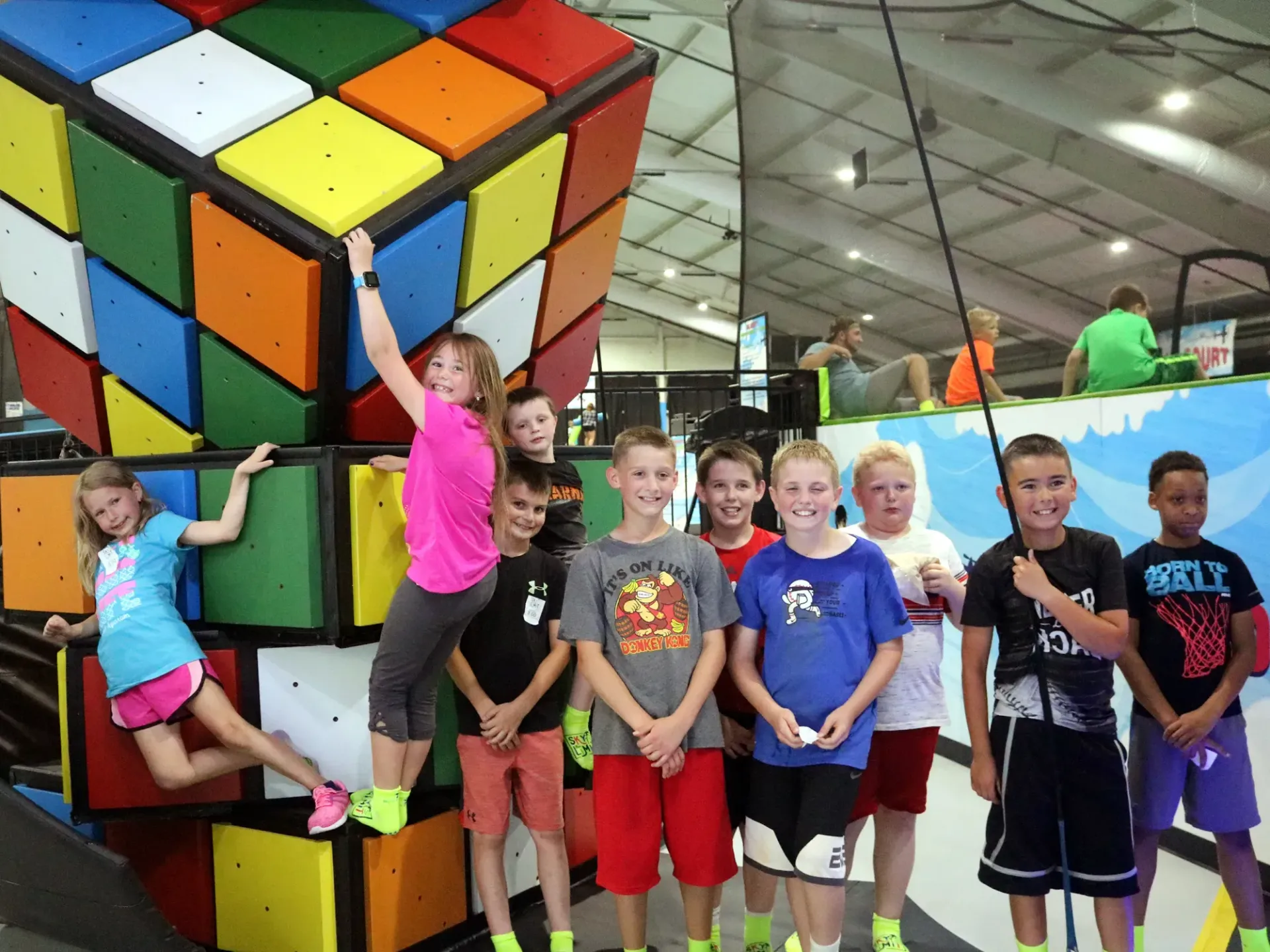 Group of children smiling near a giant, colorful Rubik's cube structure in an indoor play area.