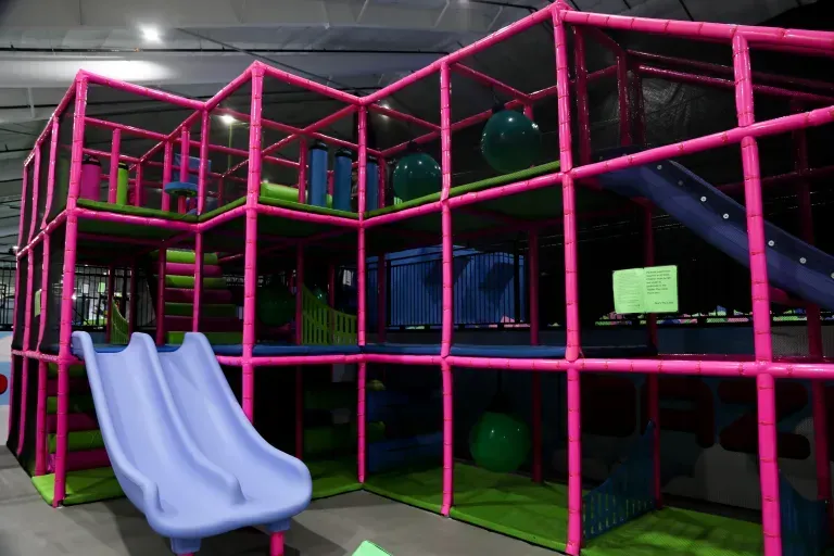 Indoor playground with pink frame, slides, platforms, and green and blue elements.