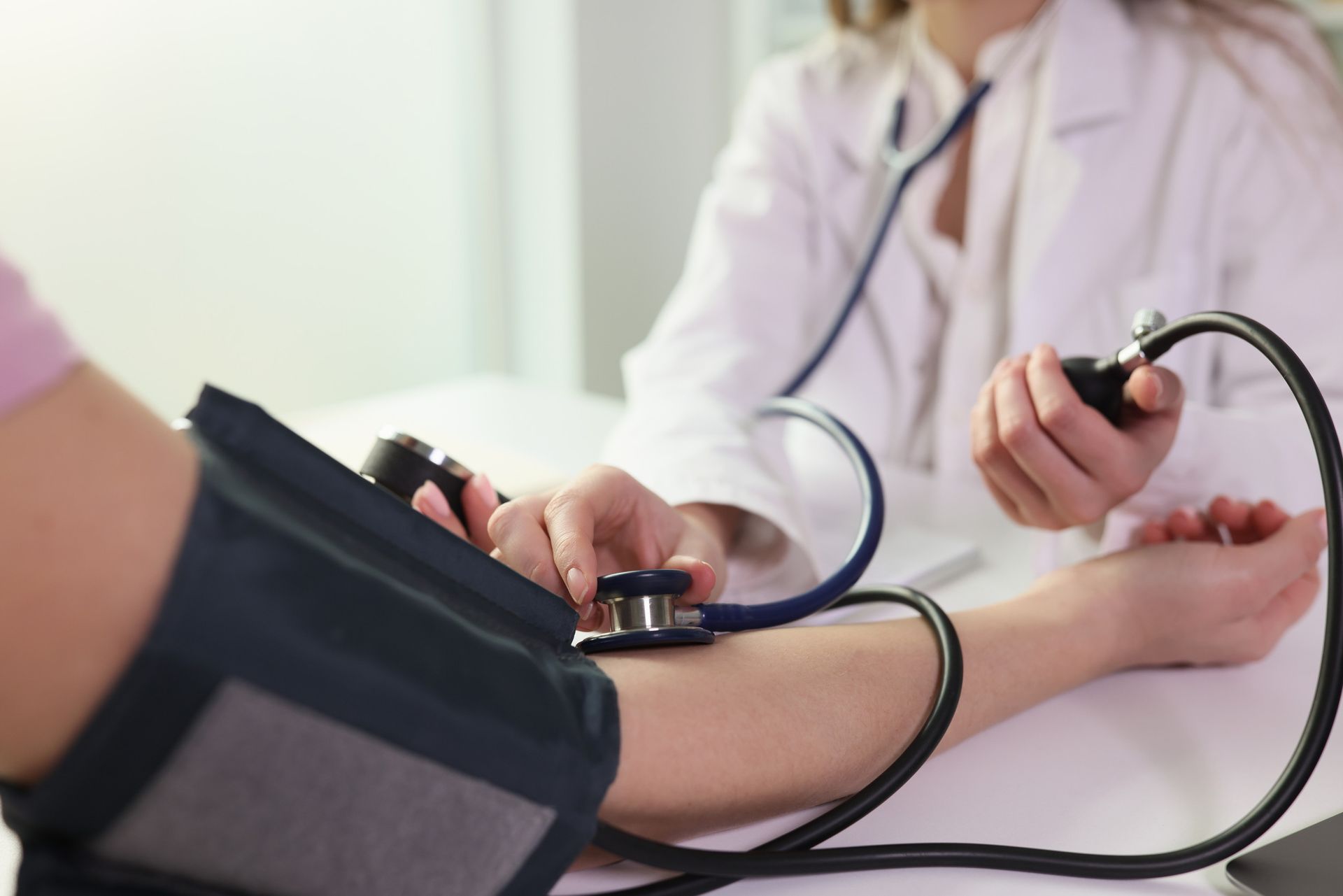 A medical professional uses a stethoscope and a blood pressure cuff to measure a patient's blood pressure in a clinic.