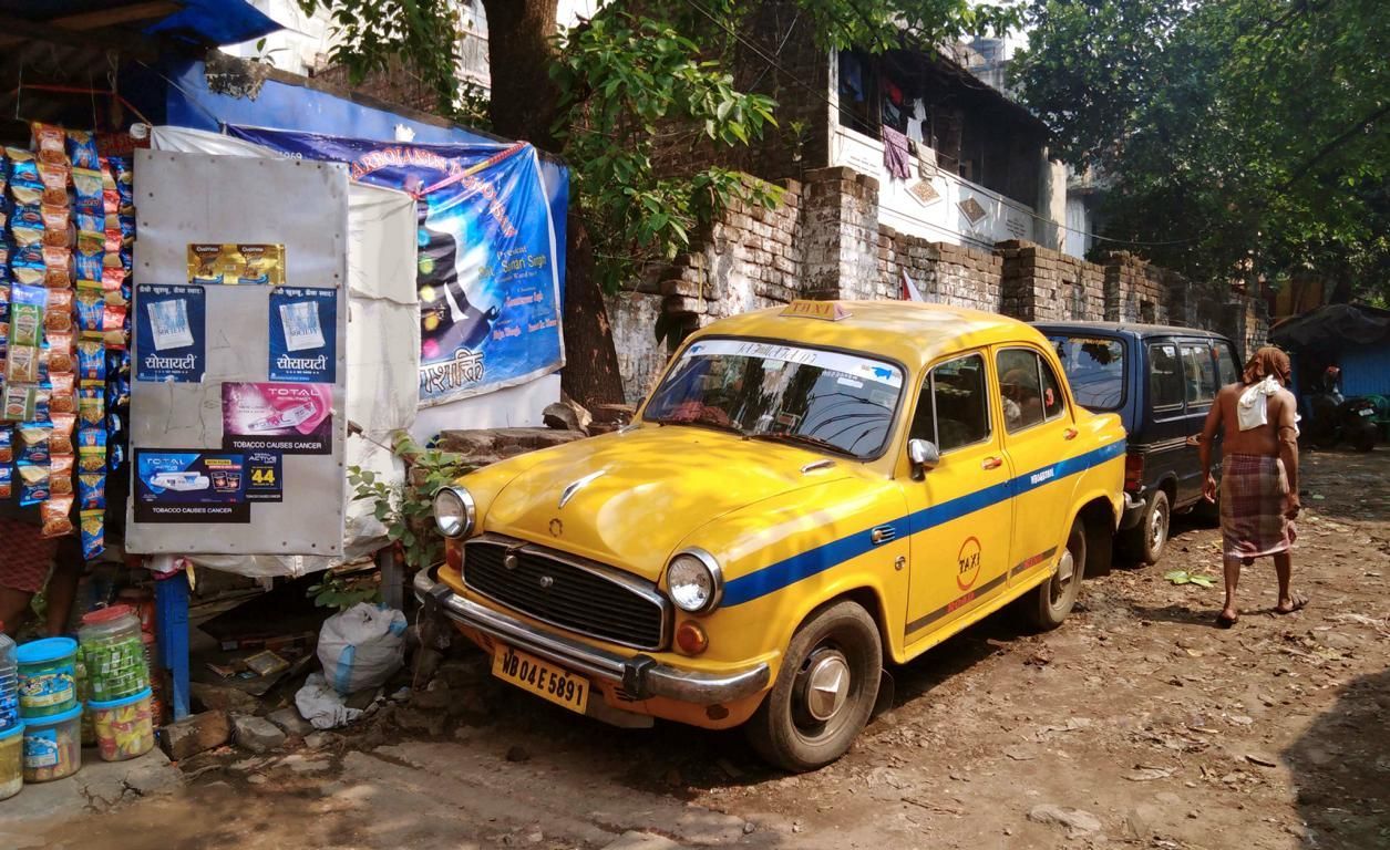 gelbes altes Taxi in Kalkutta, ein mann läuft zu einer nahe gelegenen öffentlichen Wasserentnahmestelle. 