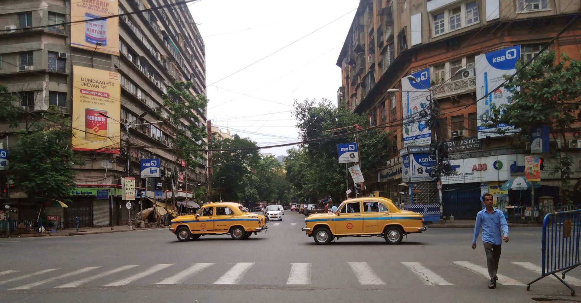 Straßenszene in Kalkutta. Zwei Taxis Überqueren eine Kreuzung, links ein Gebäude aus kommunistischer Zeit
