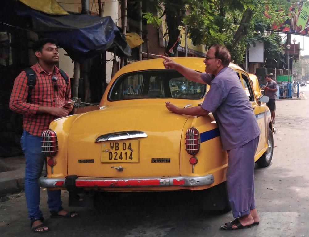 Taxi in Kalkutta. Daneben steht der Fahrer und gibt einem Passanten eine Wegbeschreibung.