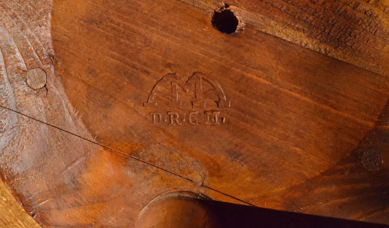 Unterseite eines antiken Elektriker-Werkstatthockers aus Holz mit Isolationsfunktion. Sichtbar ist die historische Herstellermarke AMA und die Bezeichnung D.R.G.M. (Deutsches Reichs-Gebrauchsmuster) im Buchenholz