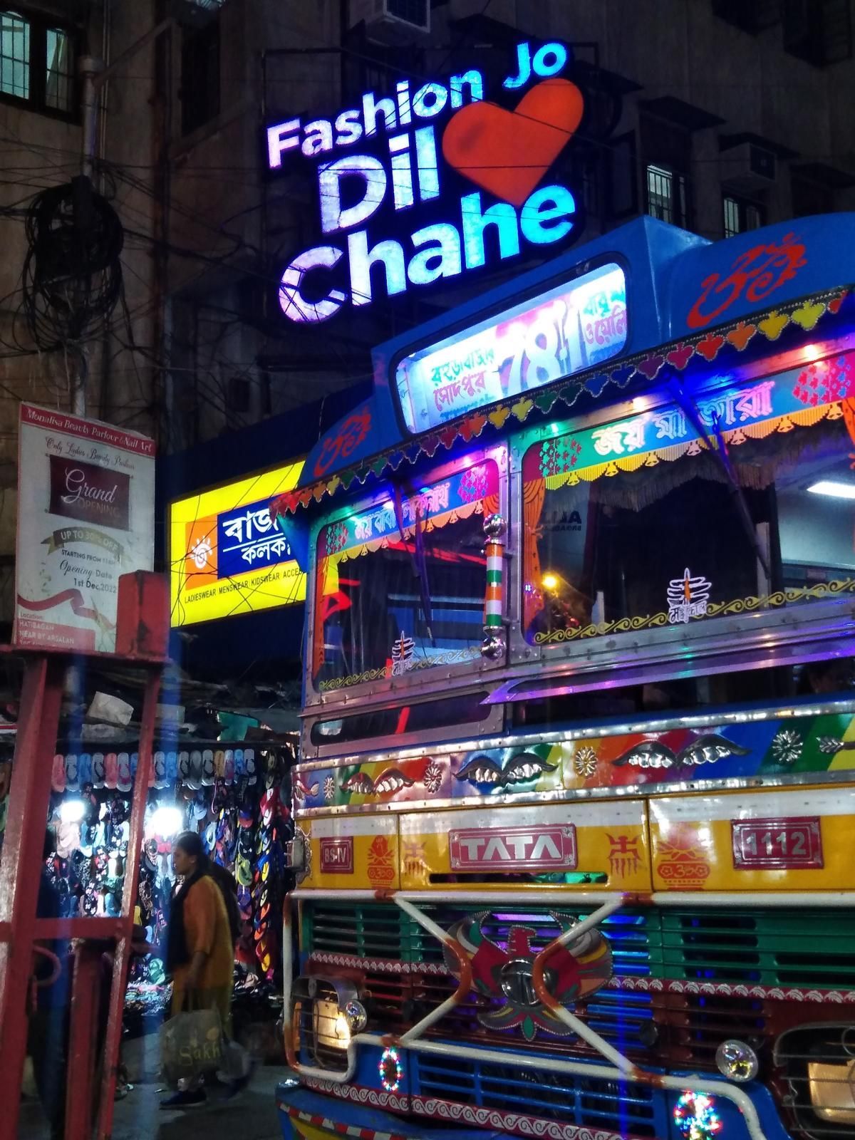 bemalter und beleuchteter Bus umgeben von Leuchtreklame in  dem Stadtteil Hanti Bagan in Kalkutta