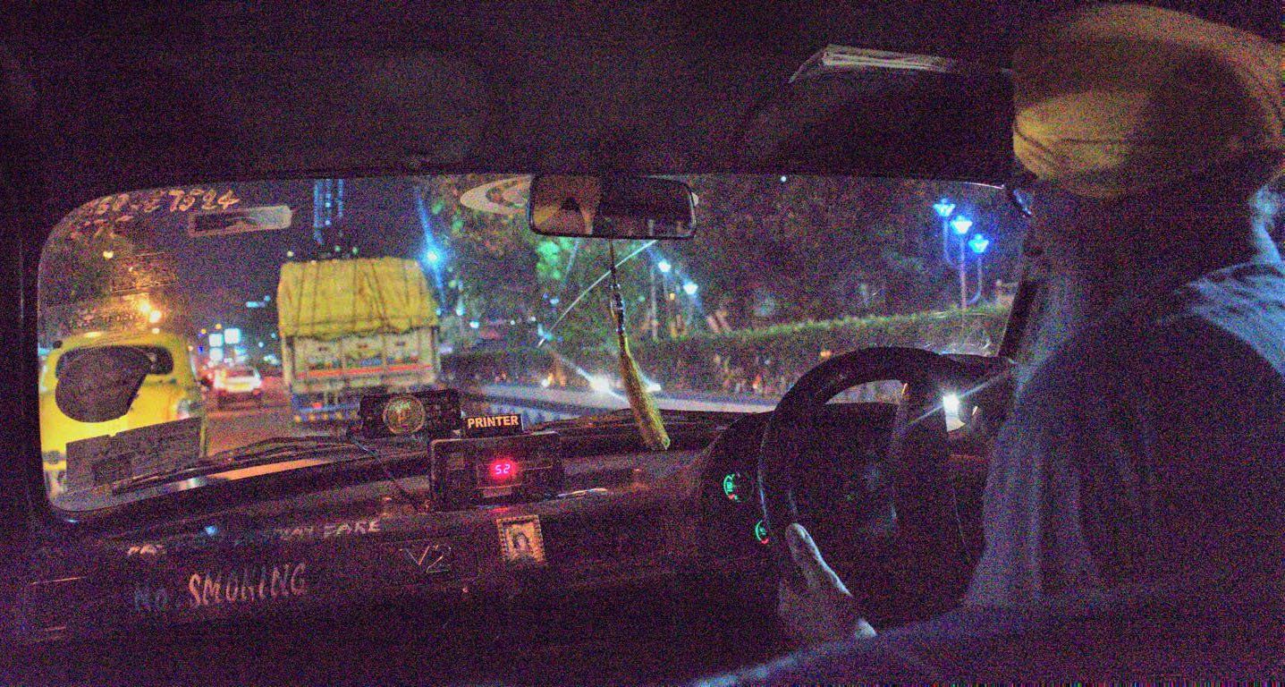 blick durch die Frontscheibe eines gelben taxis ins nächtliche Kalkutta