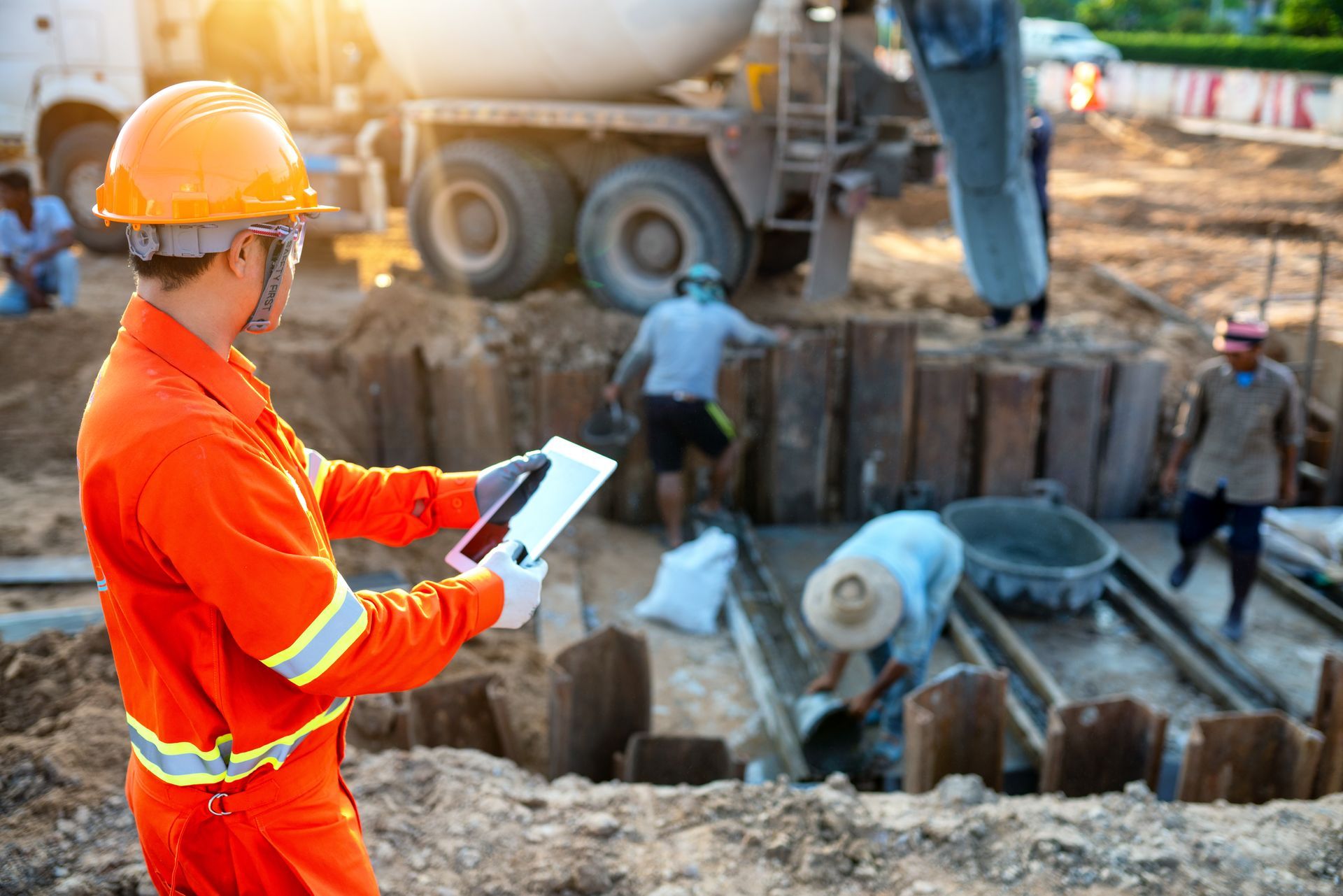 Construction supervisor using a tablet at an active excavation and concrete work site.