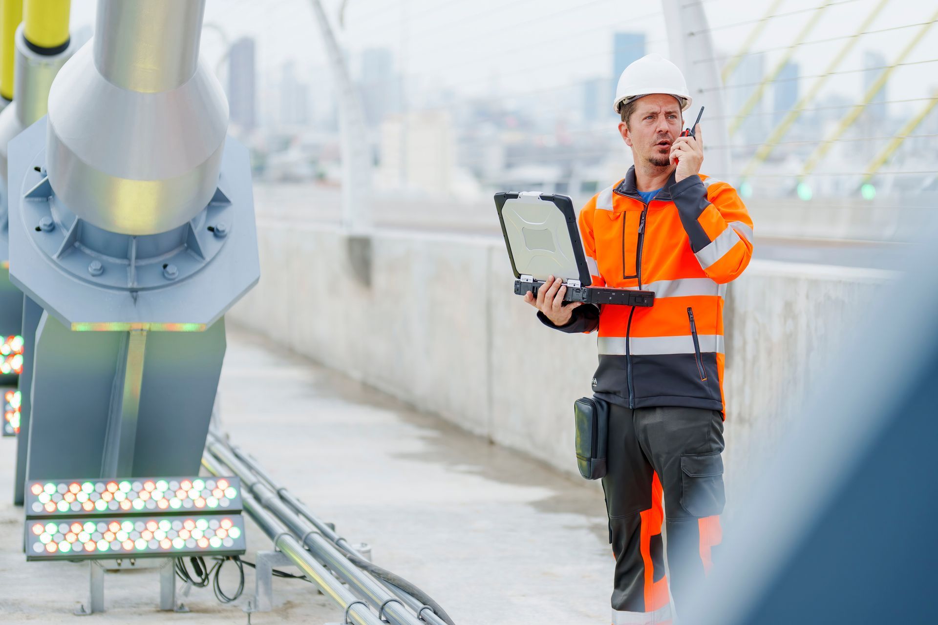 Residential structural engineer inspecting bridge supports with laptop and radio on construction site.