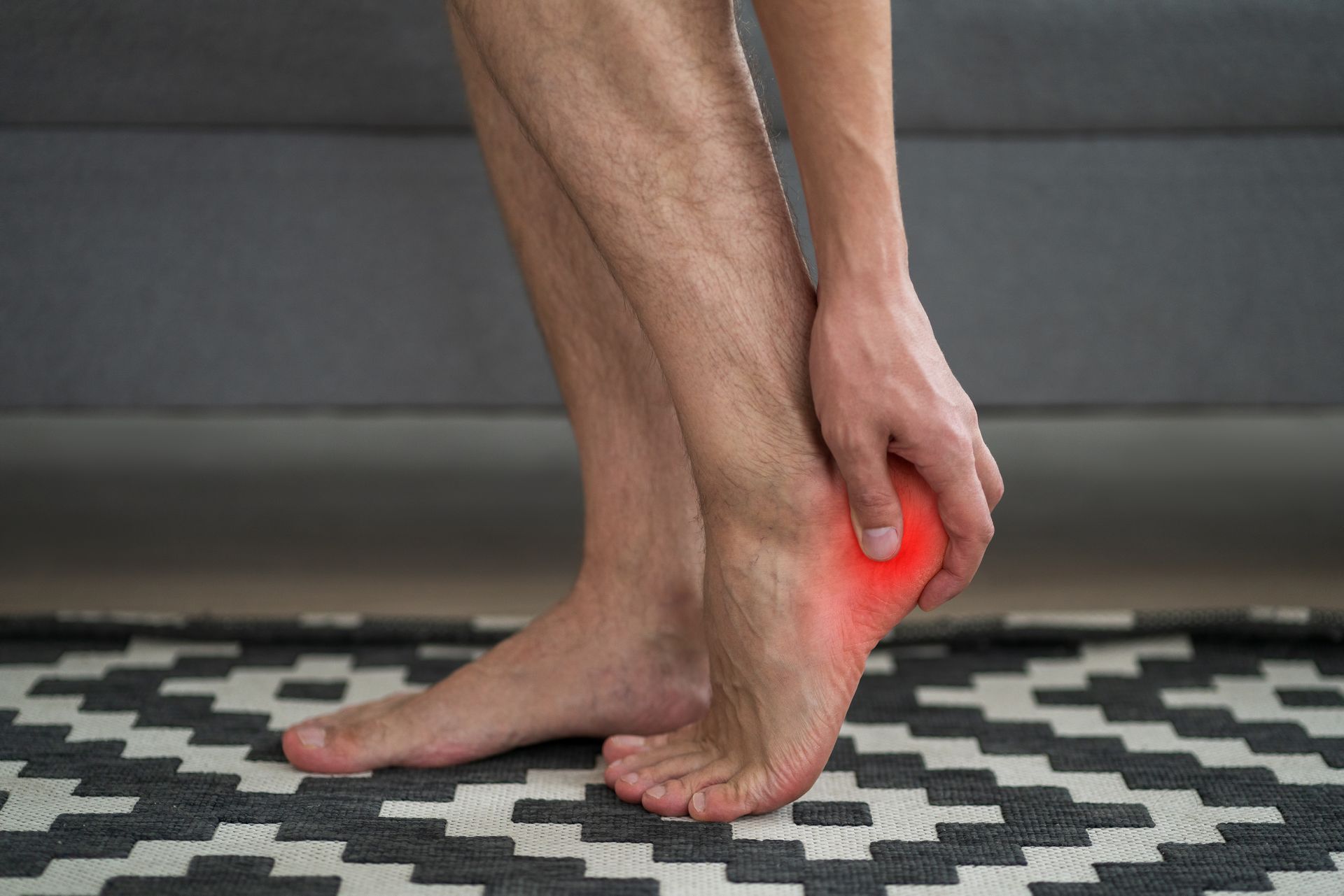 A man is holding his foot in pain on a rug.