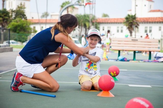 A woman is kneeling down next to a child on a tennis court.