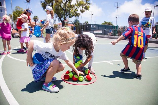 A group of children are playing with tennis balls on a court.